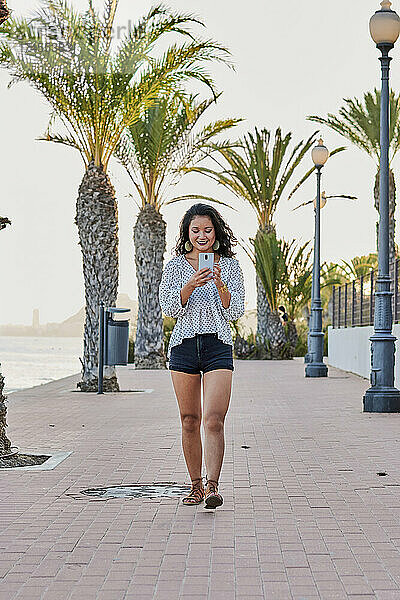 Junge asiatische Frau geht mit ihrem Handy in einer Küstenstadt spazieren