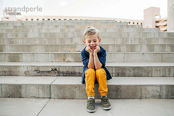 Porträt eines kleinen Jungen  der auf Betonstufen in der Innenstadt von Phoenix lacht