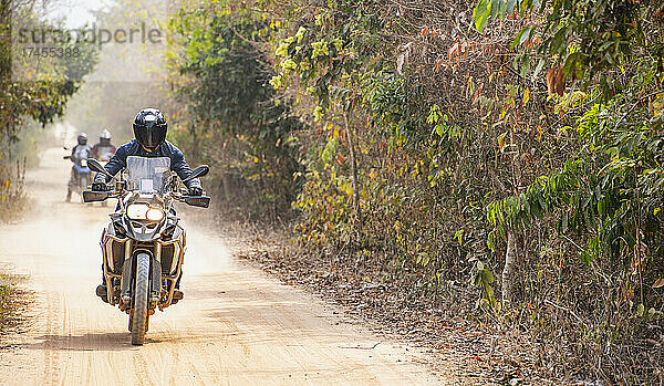 Gruppe von Männern  die mit ihrem Abenteuermotorrad auf einer unbefestigten Straße in Kambodscha unterwegs sind