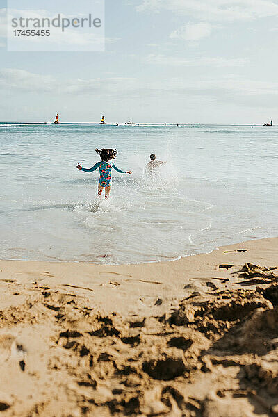 Vater und Tochter rennen am Strand von Waikiki ins Meer