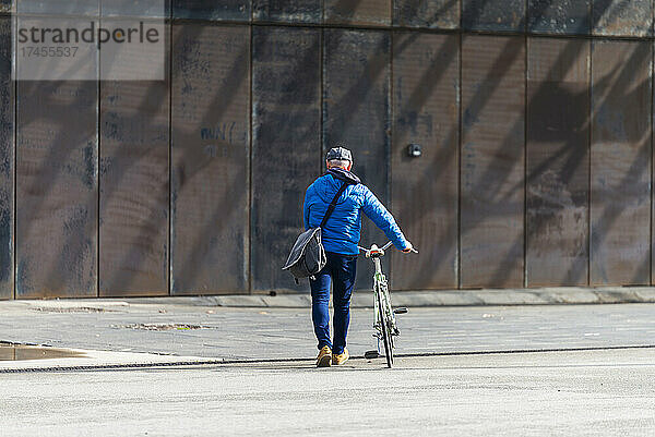 Älterer Mann fährt Fahrrad auf der Stadtstraße und hält eine Handtasche in der Hand