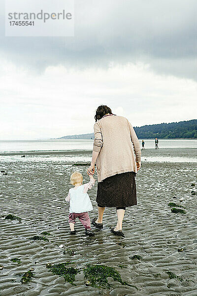 Blick von hinten auf eine Mutter und Tochter  die sich am Strand an den Händen halten