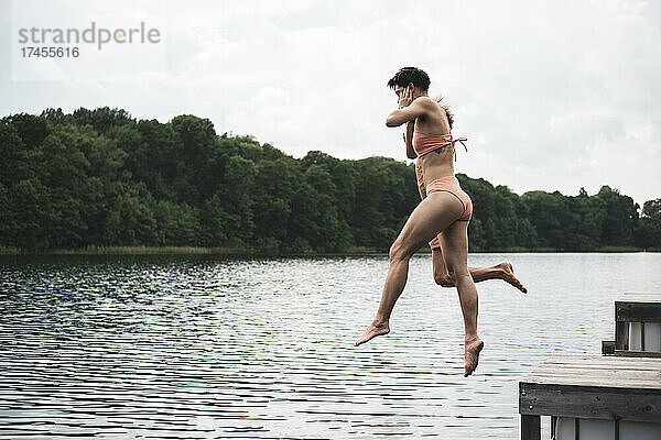 Freunde springen im Sommer im orangefarbenen Badeanzug in einen See in Polen
