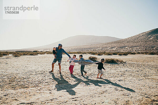 Vater und Kinder spielen am Strand von Fuerteventura und haben Spaß im Urlaub