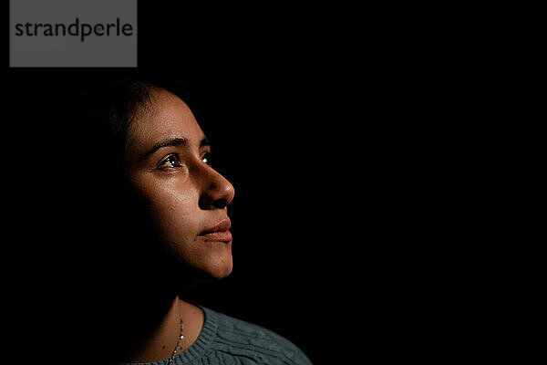Porträt einer hispanischen Frau  die im Dunkeln zur Seite schaut