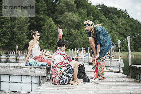 Queere Freunde genießen die Sommersonne und schwimmen auf einem Holzsteg am See