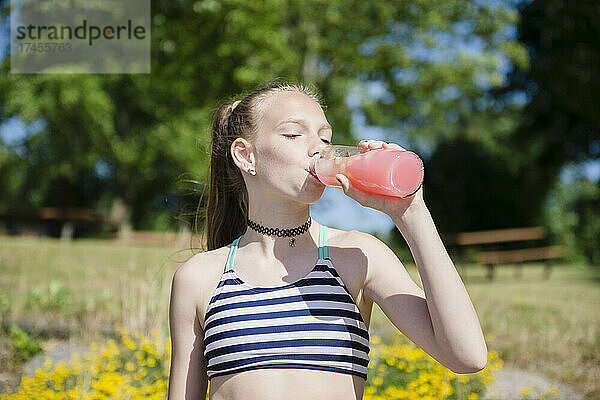 Tween-Mädchen im Badeanzug trinkt rosa Limonade im Freien.