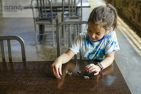 Ein kleines Mädchen sitzt an einem Tisch und spielt mit winzigen Spielzeugtieren