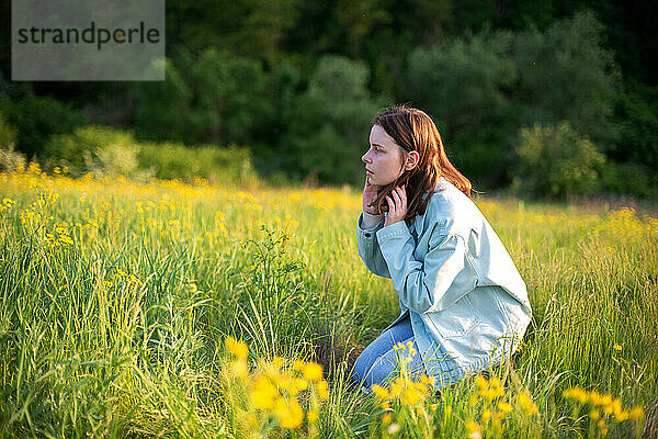 Porträt einer selbstbewussten jungen Frau  die auf dem Feld sitzt