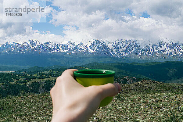 Thermoskanne mit Kaffee in der Hand. Landschaft mit Altai-Gebirge.