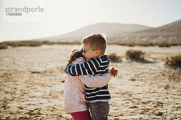 Glücklicher Bruder und Schwester  die sich bei Sonnenuntergang am Strand umarmen