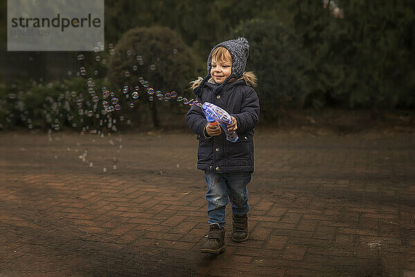 Kleinkind in warmer Kleidung spielt draußen mit Seifenblasenpistole