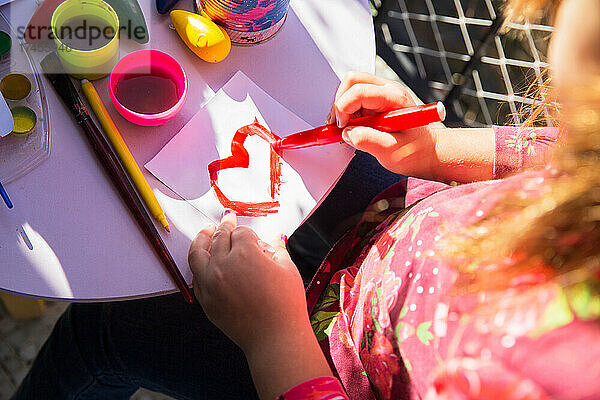 Draufsicht auf ein Kindergartenmädchen  das zum Spaß ein Herz mit einem Marker zeichnet.