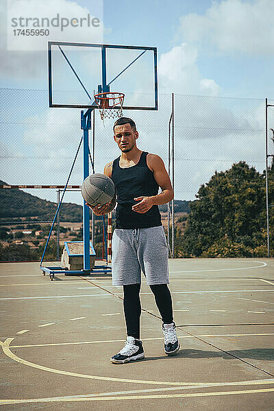 Junger tätowierter Latino-Junge spielt mit einem Basketball auf einem Platz