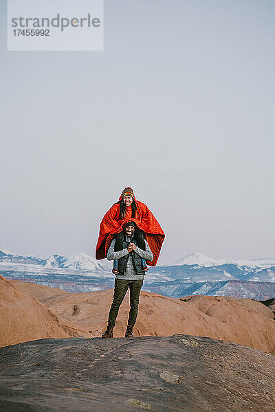 Eine Frau sitzt auf den Schultern ihrer Freundin und lacht in den Bergen