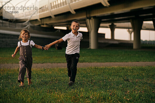 Kinder  Jungen und Mädchen  laufen Händchen haltend bei Sonnenuntergang unter der Brücke hindurch.