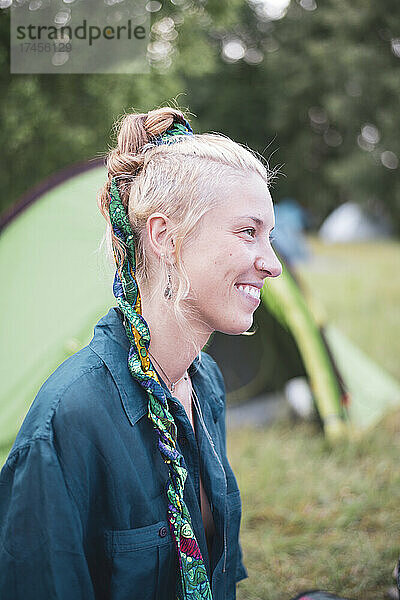 Lächelndes Porträt einer blonden Bohemienfrau mit Schleife im Haar beim Camping