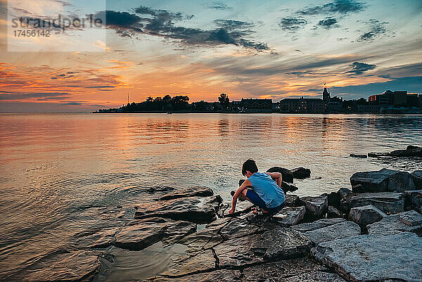 Kleines Kind spielt bei Sonnenuntergang an einem felsigen Ufer des Lake Ontario.