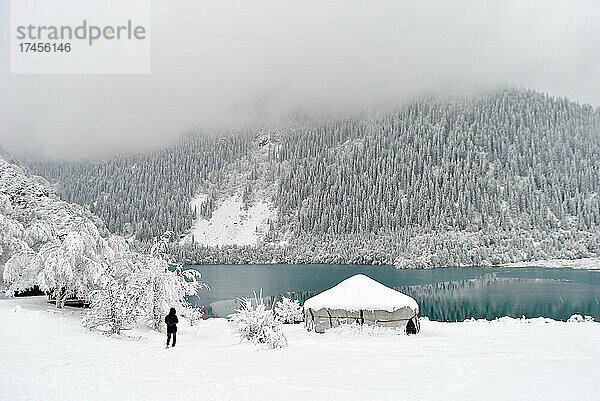 Blick aus der Ferne auf einen Mann in der Nähe eines Bergsees im Schnee im Winter