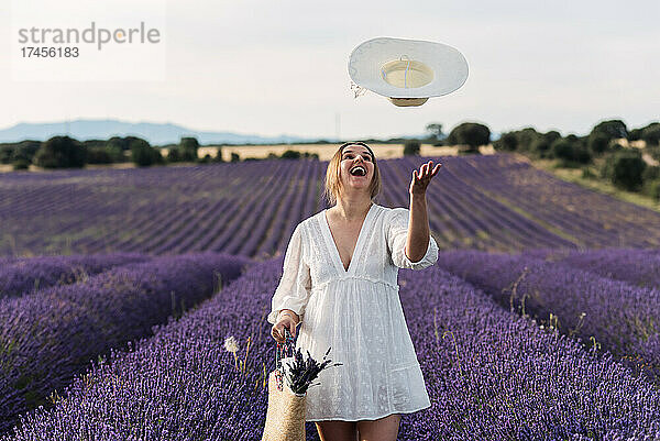 Schwangere Frau wirft ihren Hut in Lavendelfeldern in die Luft.