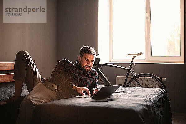 Glücklicher Mann  der zu Hause einen Laptop im Bett benutzt