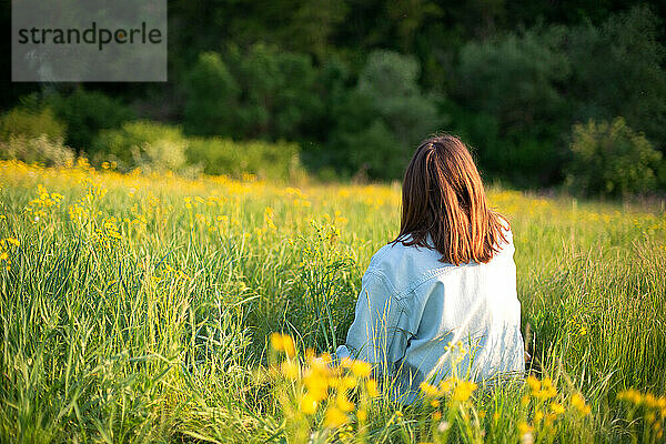 Porträt einer selbstbewussten jungen Frau  die auf dem Feld sitzt