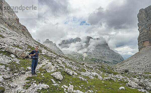 Wanderer  Bergsteiger auf einem Wanderweg zwischen wolkenverhangenen felsigem Gebirge am Forcella Grande  Sorapiss Umrundung  hinten Berg Punte Tre Sorelle  Dolomiten  Belluno  Italien  Europa