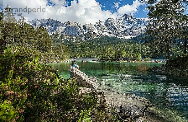 Junger Mann sitzt auf einem Felsen  Blick in die Ferne  Eibsee und Zugspitze im Frühlingmit Schnee  Wettersteingebirge  bei Grainau  Oberbayern  Bayern  Deutschland  Europa