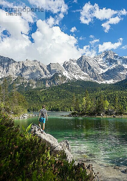 Junger Mann steht auf einem Felsen  Blick in die Ferne  Eibsee und Zugspitze im Frühlingmit Schnee  Wettersteingebirge  bei Grainau  Oberbayern  Bayern  Deutschland  Europa