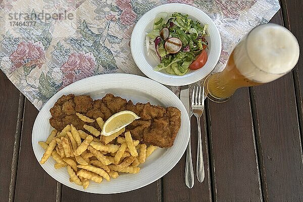 Schnitzel mit Pommes frites  Salatteller und ein Weizenbier auf einem Teller in einem Biergarten serviert  Bayern  Deutschland  Europa