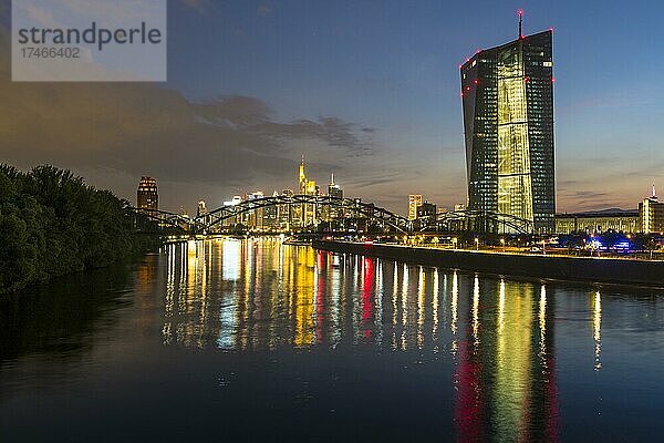 Beleuchtete Europäische Zentralbank  EZB und bunt strahlende Skyline von Frankfurt spiegeln sich im Main wärend der späten Abenddämmerung vom Arthur-von-Weinberg-Steg aus  Frankfurt am Main  Hessen  Deutschland  Europa