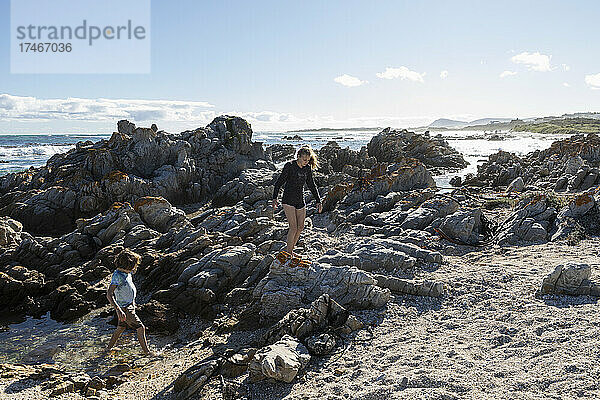 Zwei Kinder  ein Mädchen im Teenageralter und ein achtjähriger Junge  erkunden die zerklüfteten Felsen und Felstümpel an einem Strand.