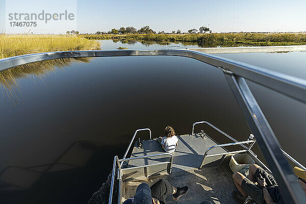 Ein Junge auf einem Motorboot fährt auf einer Wasserstraße im Okavango-Delta