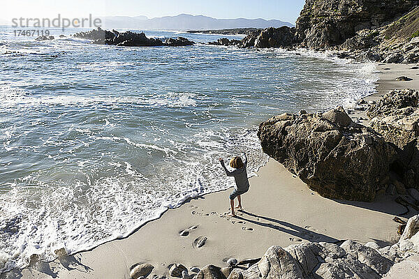 Ein kleiner Junge allein auf einem kleinen Stück Sand unter den Klippen am Meer.