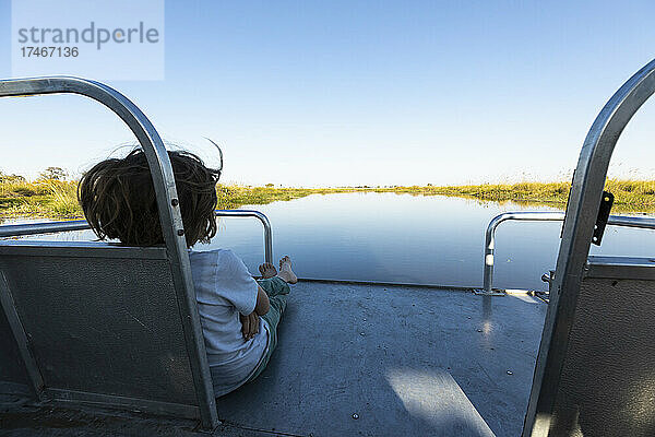 Ein Junge auf einem Motorboot fährt auf einer Wasserstraße im Okavango-Delta