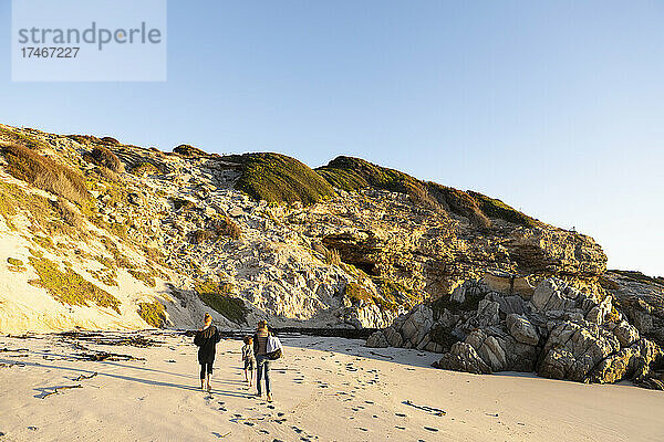 Eine Familie spaziert am Sandstrand entlang in Richtung der Klippen.