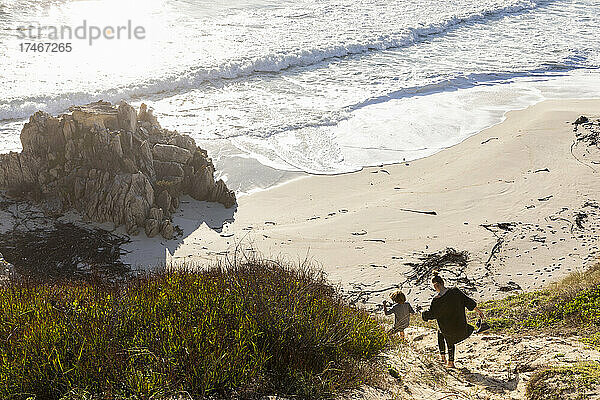 Ein Mädchen im Teenageralter und ihr Bruder rennen einen Weg hinunter zu einem Sandstrand