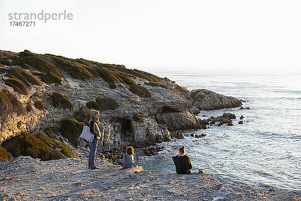 Drei Personen  eine Familie  die den Sonnenuntergang über dem Meer beobachtet.