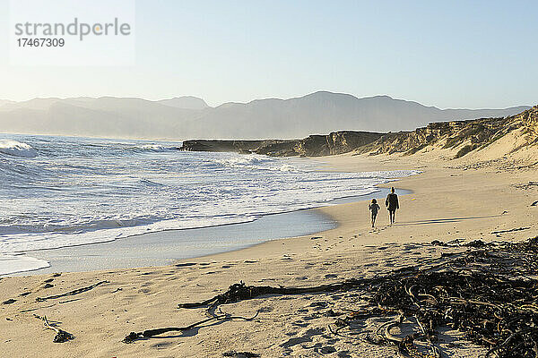 Zwei Personen  die an einem Sandstrand spazieren gehen  ein Teenager und ein Junge