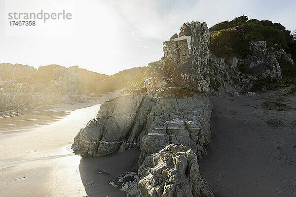 Zwei Kinder klettern auf den Felsen oberhalb eines Sandstrandes.