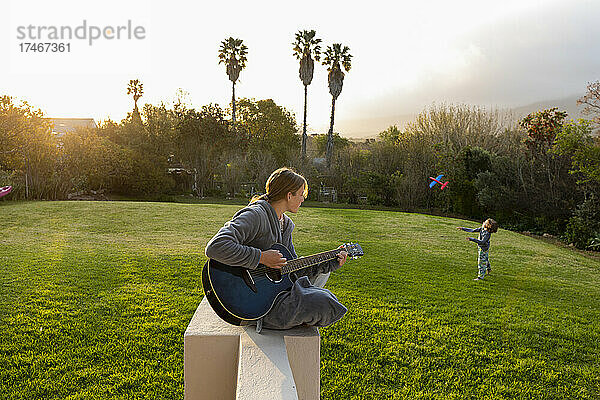 Teenager-Mädchen spielt Gitarre und singt im Freien
