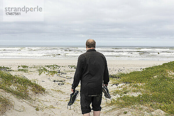 Ein reifer Mann  der mit seinen Schuhen in der Hand über einen Strand läuft