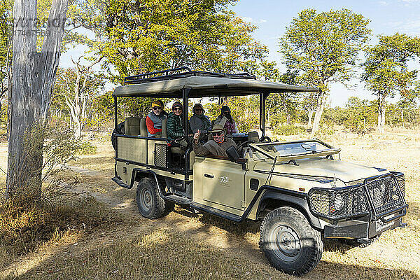 Ein Safari-Jeep  der im Schatten eines Baumes geparkt ist und in dem Menschen sitzen.