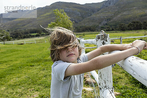 Achtjähriger Junge lehnt an einem Zaun und sieht sich Pferde auf einem Feld an