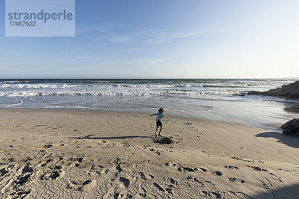 Kleiner Junge  der an einem Strand an der Atlantikküste im Freien läuft.