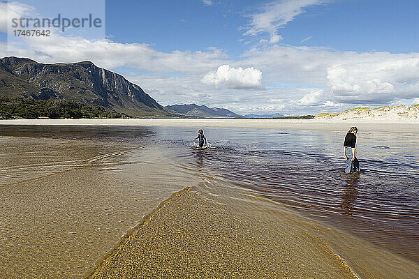 Teenager-Mädchen und Junge an einem offenen Sandstrand  die durch flaches Wasser waten.
