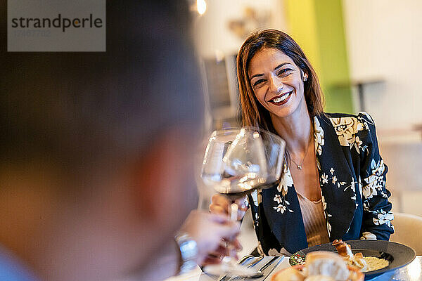 Lächelnde Frau prostet Weinglas mit Mann im Restaurant an