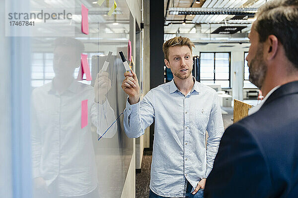 Junger Geschäftsmann mit Stift erklärt Kollege über Diagramm am Whiteboard