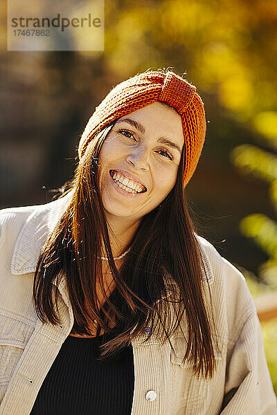 Lächelnde schöne junge Frau mit Strickmütze an einem sonnigen Tag