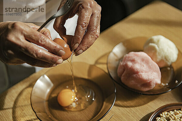 Frau zerbricht Ei in Schüssel in der Küche